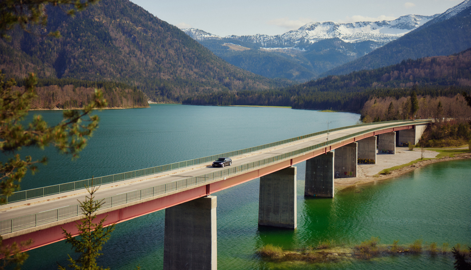 Auto fährt auf einer Brücke, im Hintergrund Berge